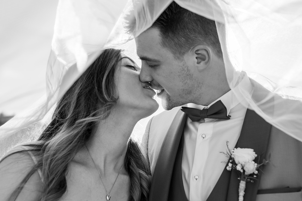 Couple s'embrassant sous un voile devant l'objectif d'un photographe professionnel lors d'une cérémonie de mariage
